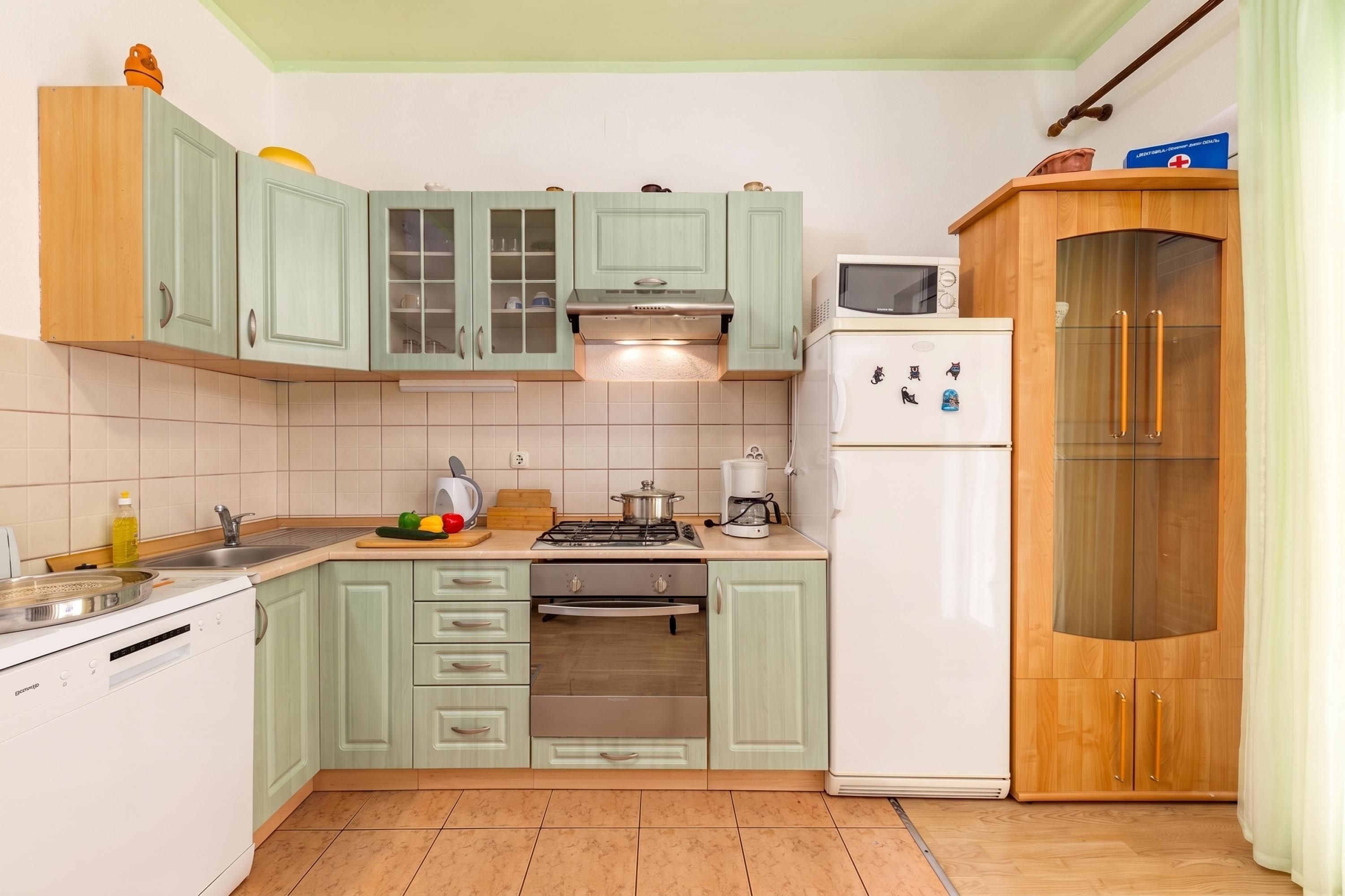 Una cocina compacta con gabinetes verde claro, un refrigerador blanco, una estufa y un microondas.