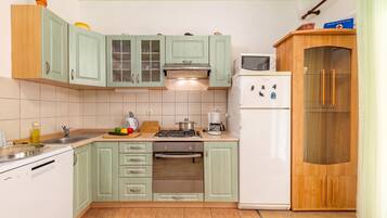 Una cocina compacta con gabinetes verde claro, un refrigerador blanco, una estufa y un microondas.