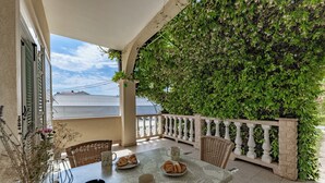 A balcony with a table set for breakfast, including croissants and coffee cups, and a lush green wall. - Apartmani Mijatović (Lopar)