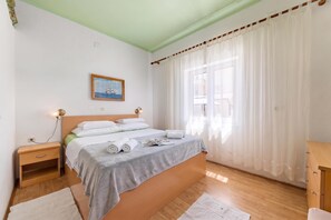 Un dormitorio con cama, mesitas de noche, una ventana con cortinas y un cuadro en la pared.