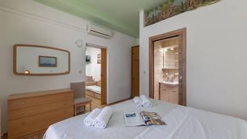 A hotel room with a bed, a wooden dresser, a mirror, and a door leading to a bathroom.