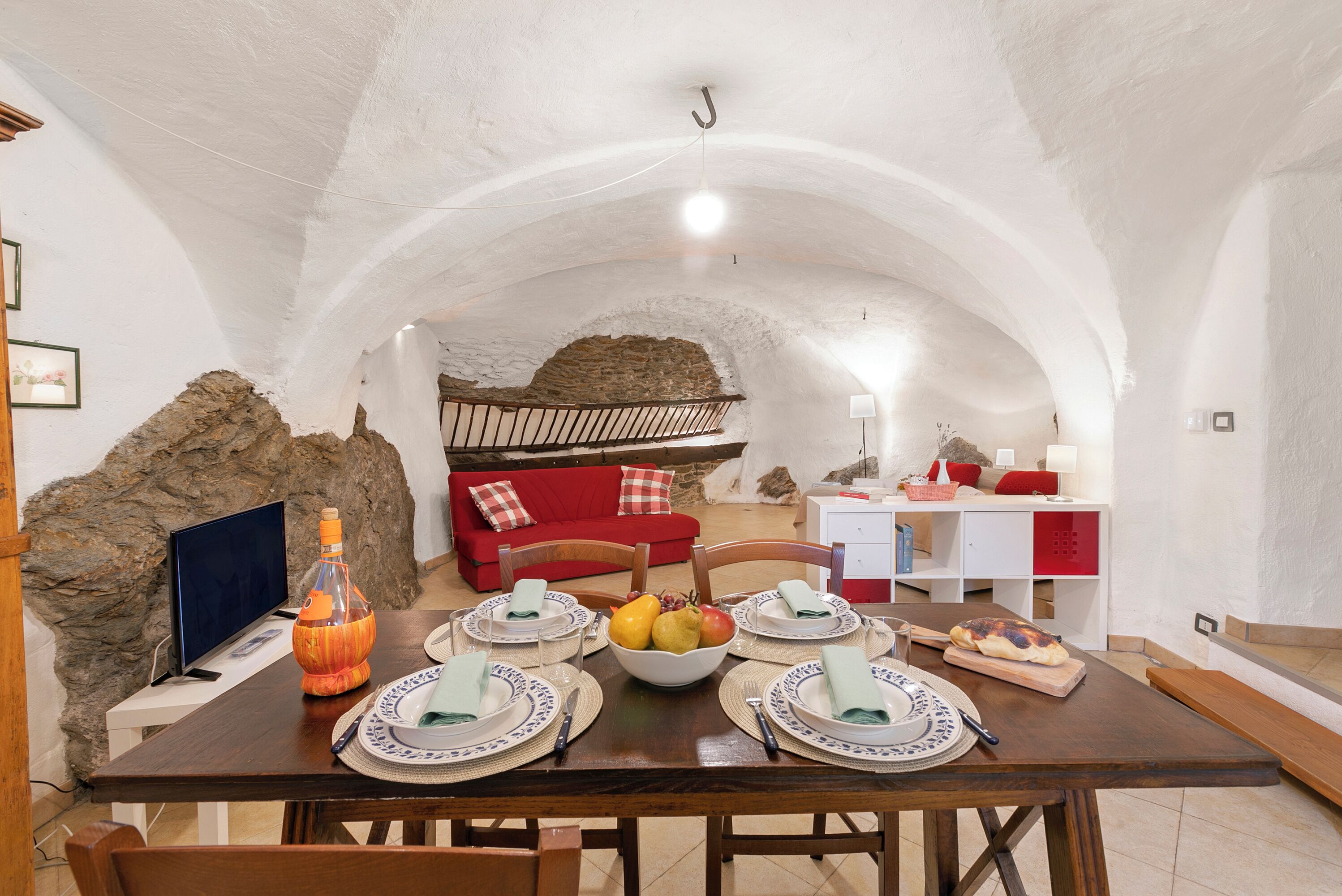 A dining area with a stone wall, a red sofa, and a wooden table set for four.