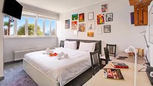 Habitación de hotel con cama, escritorio, silla, televisor y obras de arte en las paredes.