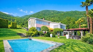 Una casa moderna con piscina, rodeada de abundante vegetación y colinas.