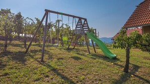 A playground with a swing set and a slide, surrounded by grass and trees. - Vineyard Cottage Brodaric (Metlika)