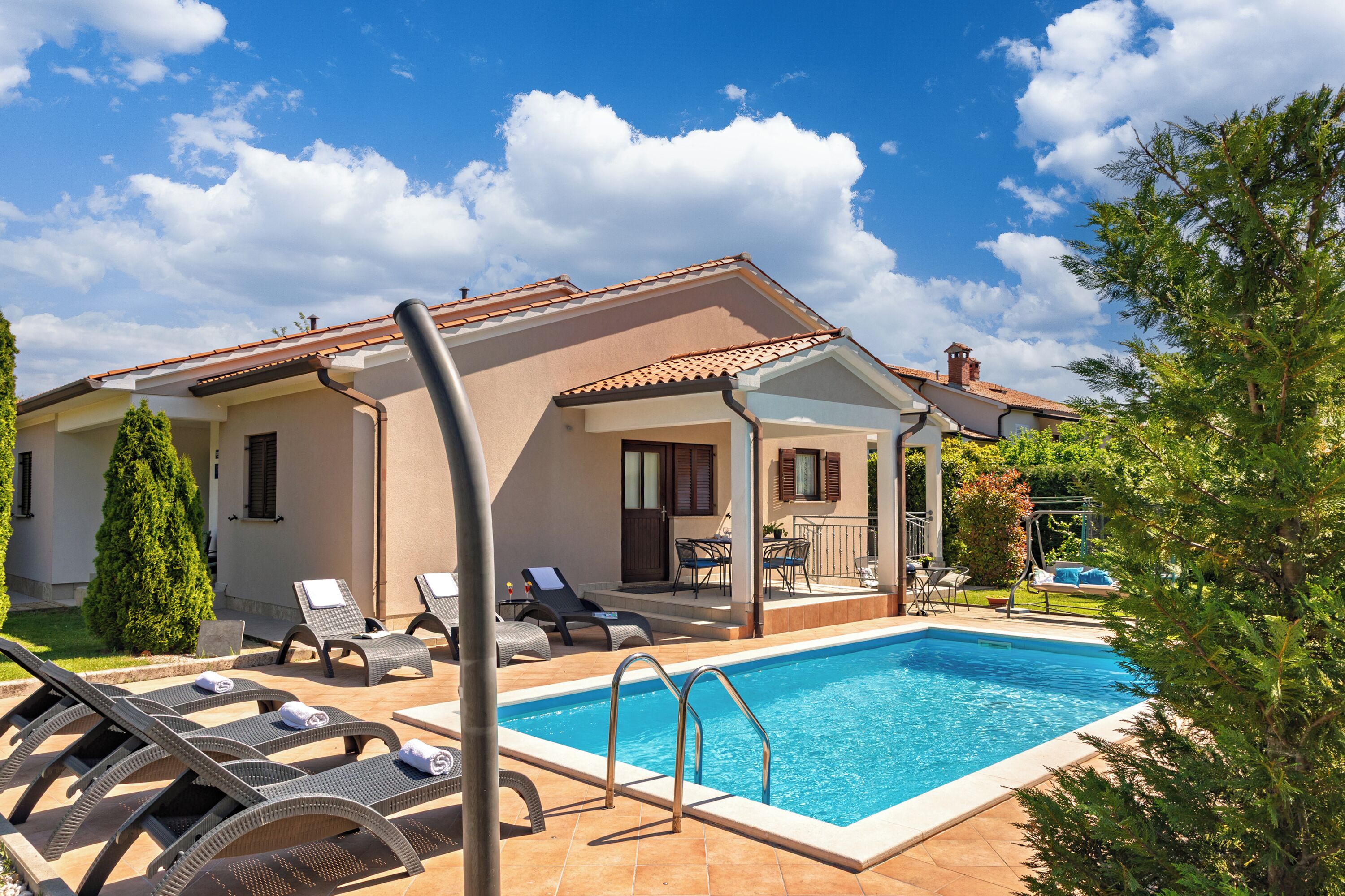 Ein Poolbereich mit Liegestühlen, einer überdachten Terrasse und blauem Himmel.