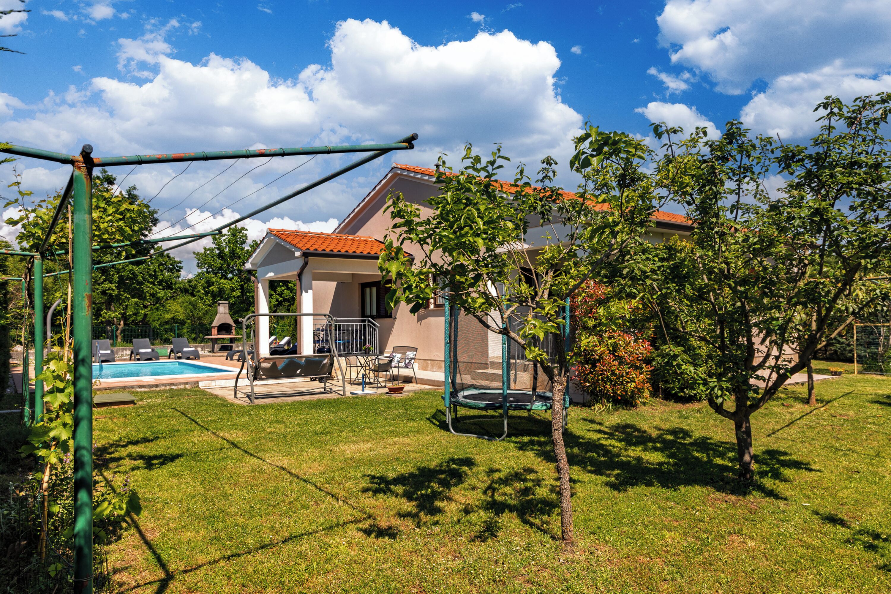 A house with a swimming pool, a trampoline, and a fenced yard.