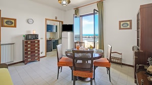 Un coin repas avec une table ronde, des chaises, un téléviseur et une vue sur la mer.