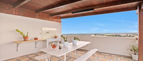 Une terrasse sur le toit avec un plafond en bois, une table blanche avec des bancs, des plantes en pot et une vue dégagée sur le paysage.