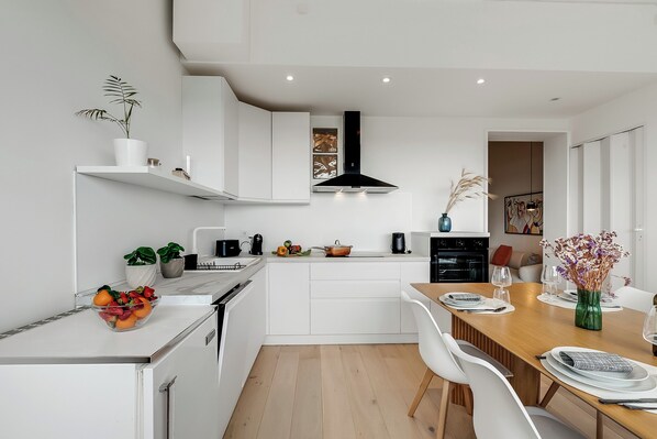 A modern kitchen with white cabinetry, a wooden dining table, and a black range hood. - Sky View Apartment Monopoli (Monopoli)