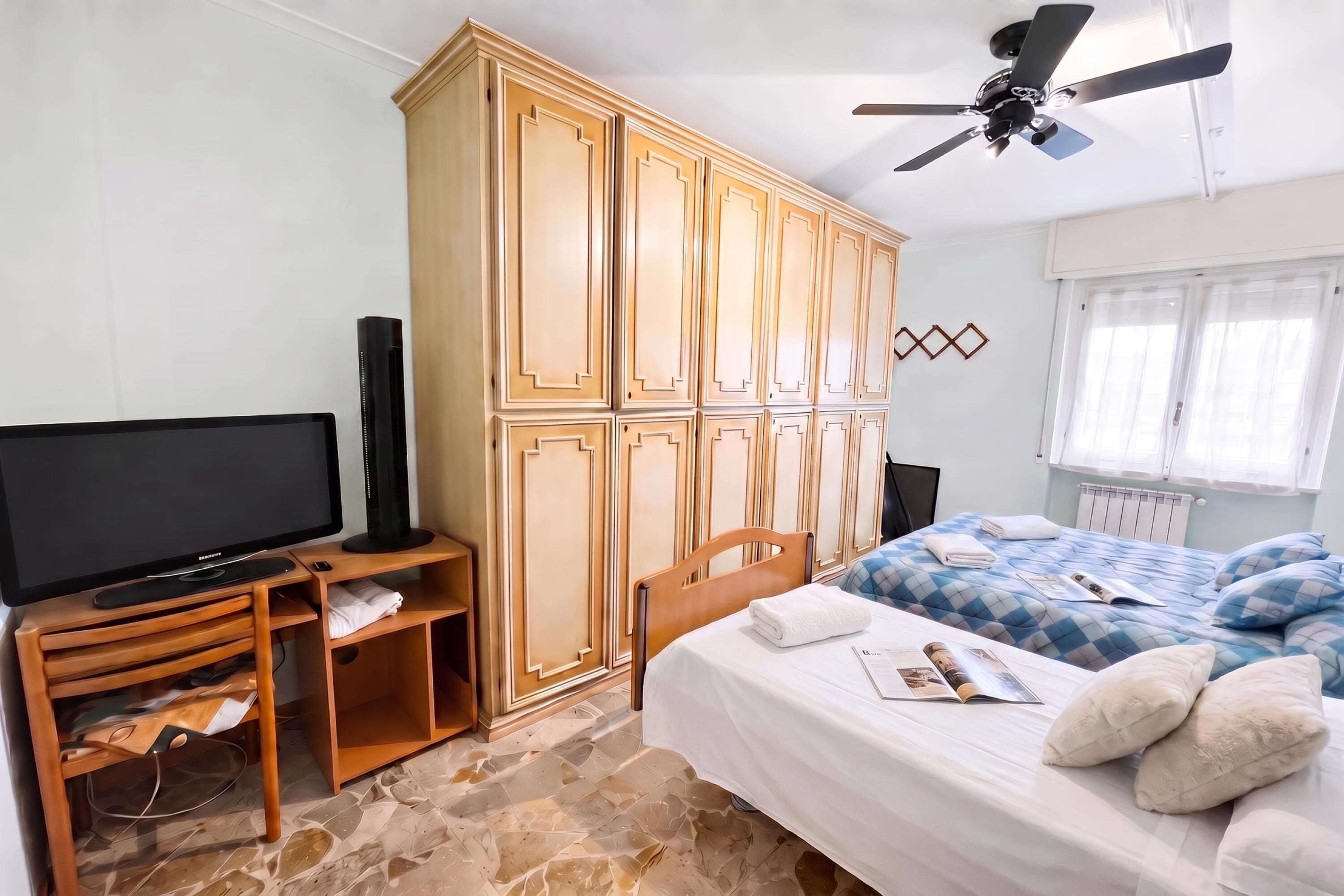 Un dormitorio con cama, televisión, armario y ventilador de techo.
