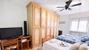 Quarto com cama, televisão, guarda-roupa e ventoinha no teto.