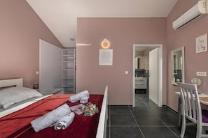 Hotellihuone, jossa on sänky, punainen heittopeitto, pyyhkeet, maljakko täynnä kukkia, peili ja ovi, joka johtaa kylpyhuoneeseen.