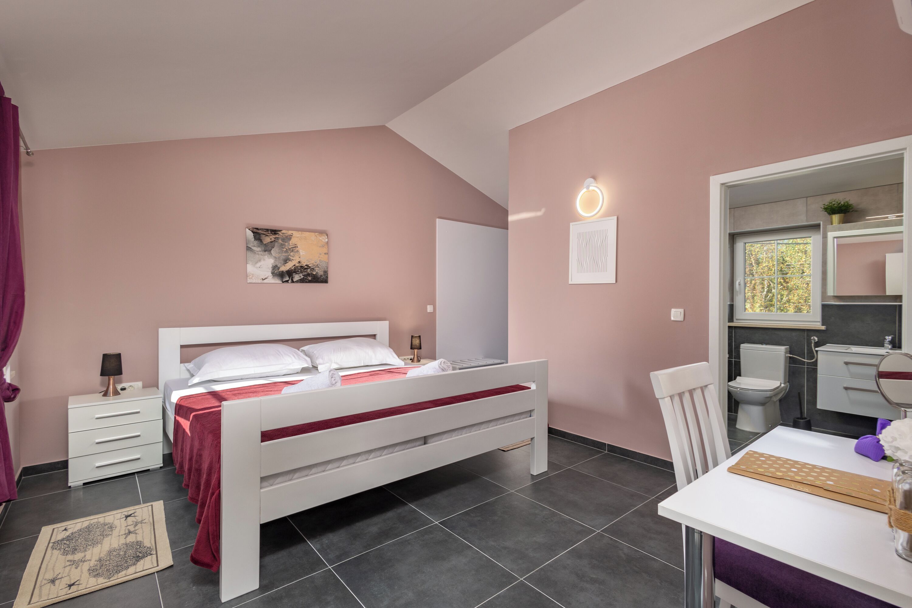 A bedroom with a bed, bedside table, lamp, and a small desk with a chair.