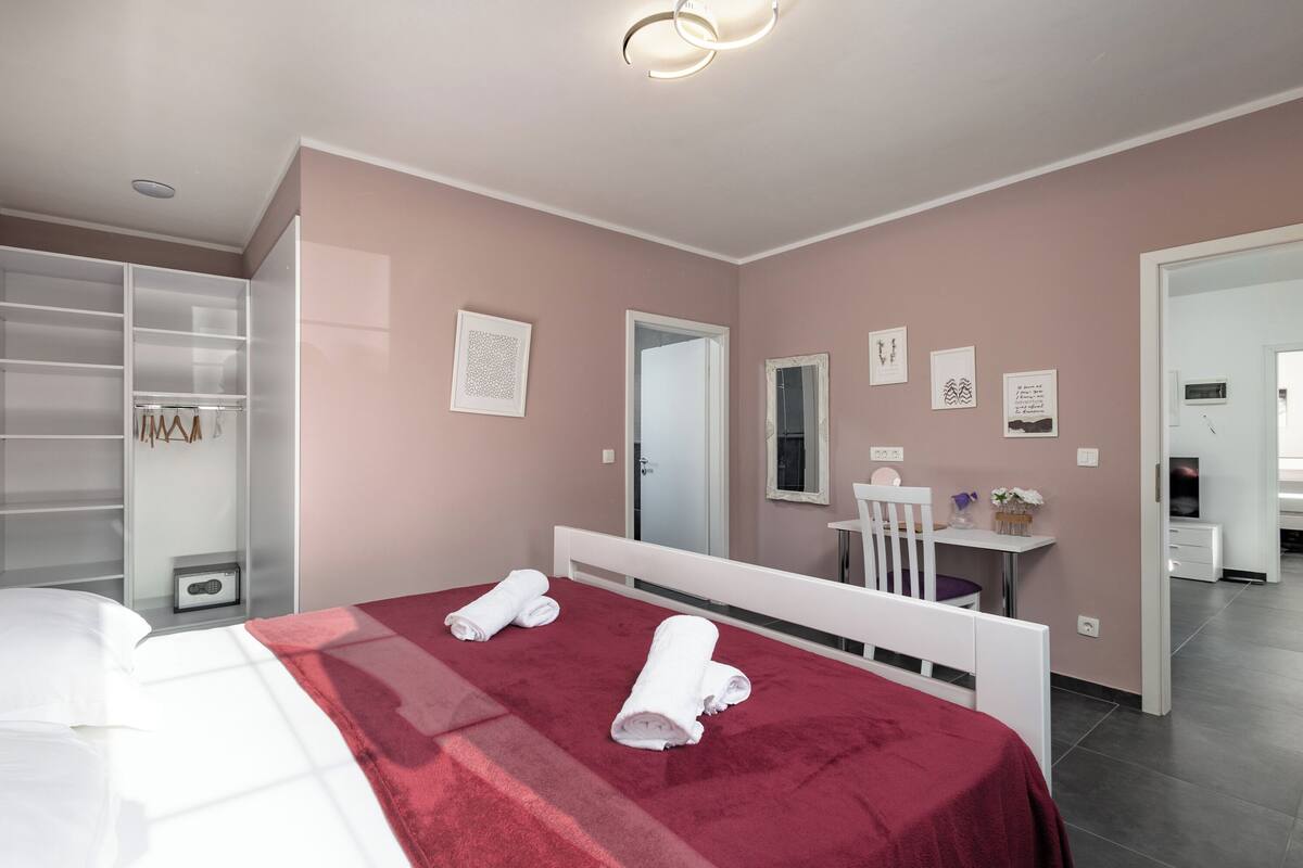 A modern bedroom with a bed, a wardrobe, a desk, and a bathroom visible in the background.
