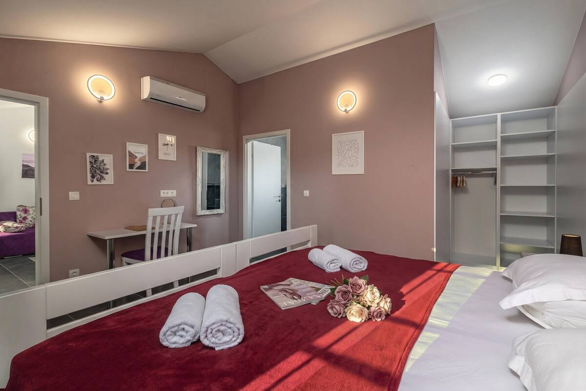 A hotel room with a bed, a desk, a chair, a wardrobe, and a mirror.