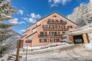 A multi-story building with balconies, a garage, and a snowy landscape. - Appartamento Quota 1800 for 4 + ski Storage (Claviere)
