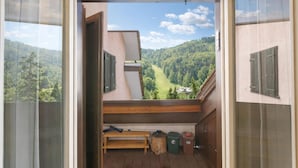 A balcony with a view of a forested valley, a wooden bench, and a small table with a broom. - Appartamento Quota 1800 for 4 + Garage + ski Storage (Claviere)
