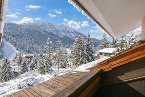 A wooden deck overlooking a snowy mountain landscape with buildings and trees.