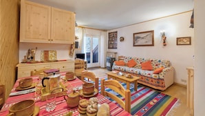 A cozy living room with wooden furniture, a colorful sofa, and a dining area with wooden cups and a coffee pot. - Appartamento Quota 1800 for 4 + Garage + ski Storage (Claviere)