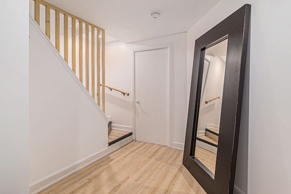 Un pasillo con una escalera de madera, una puerta blanca y un espejo en la pared.