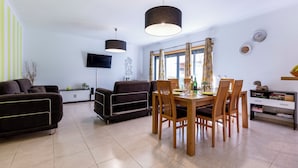 Ett modernt vardagsrum med en soffa, ett matbord med stolar, en tv som är monterad på väggen och ett fönster med gardiner.