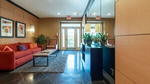 A hotel lobby with a reception desk, a red sofa, a coffee table, and framed artwork on the wall.
