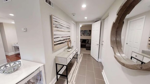 A hallway with a white console table, a large abstract painting, a mirror, and a door leading to a living area.