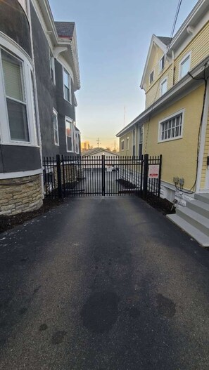 A gated driveway leading to a residential area with houses on either side.