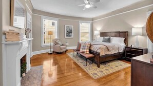 Quarto com cama, cadeira, mesa de cabeceira, luminária, lareira e ventilador de teto.