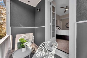 Ein Balkon mit weißer Reling, einem kleinen Tisch und zwei weißen Stühlen.