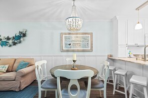 Un comedor con una mesa redonda, sillas blancas, una araña y un cuadro en la pared.