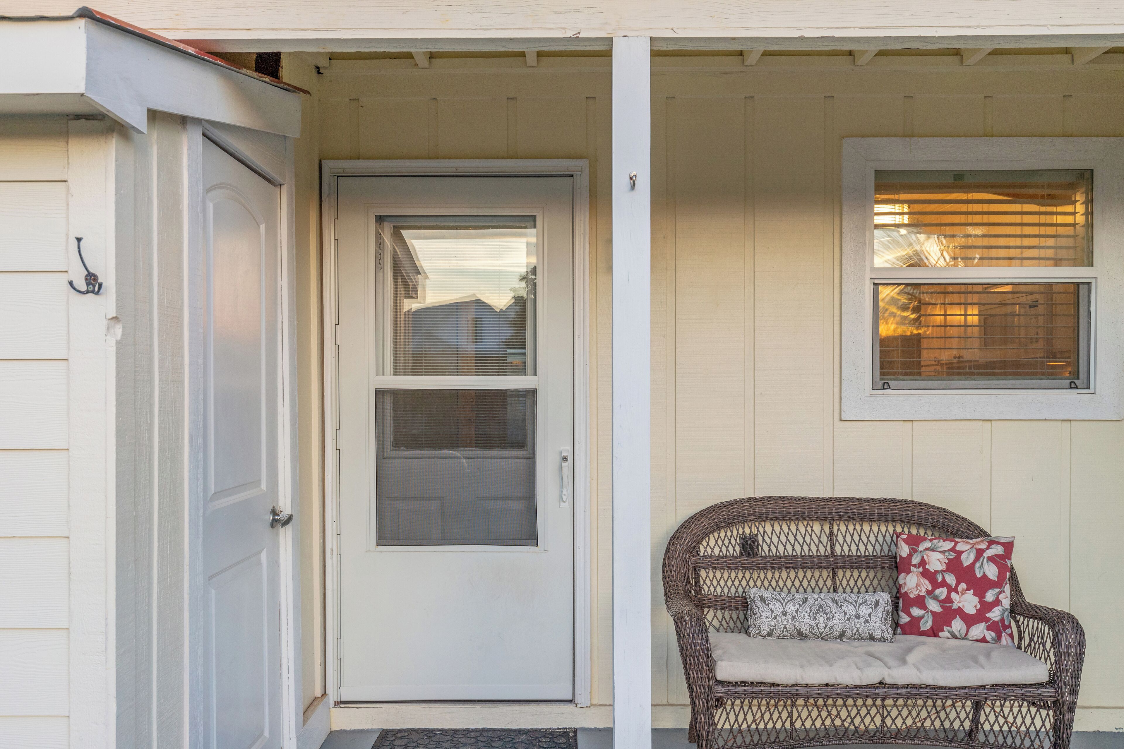 A front door with a glass panel, a wicker bench with cushions, and a window with blinds.