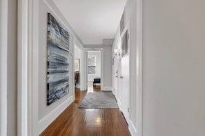 A hallway with wooden flooring, white walls, and a gray rug.