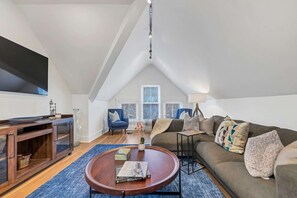 A modern living room with a high ceiling, a flat-screen TV, a sofa, a coffee table, and a fireplace. - Luxurious 2 Bdrm 2 Bath 3rd floor (Cincinnati)