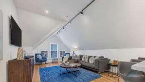 Ein geräumiges Loft-Apartment mit hoher Decke, einem großen Fenster, einem Sofa, einem Couchtisch und einem an der Wand befestigten Fernseher.