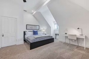 A bedroom with a bed, a desk, and a white door.