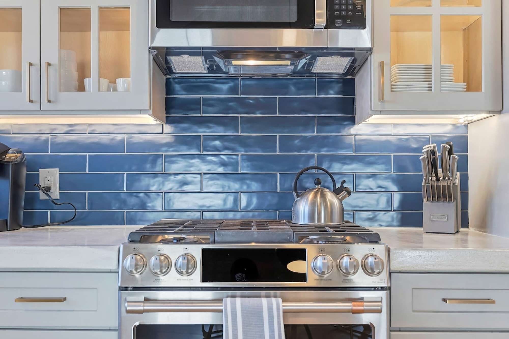A kitchen with a gas stove, oven, microwave, and a kettle.
