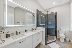 A modern bathroom with a large mirror, two sinks, a toilet, and a glass-enclosed shower.