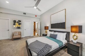A bedroom with a bed, bedside tables, a ceiling fan, and artwork on the walls.