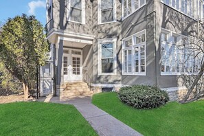 Ein zweigeschossiges Haus mit Veranda, kleinem Vorgarten und einem Maschendrahtzaun.