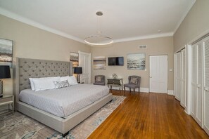Ein Schlafzimmer mit einem großen Bett, einem Schreibtisch, einem Stuhl, einem Fernseher und einem Kleiderschrank.