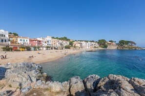 A coastal town with buildings along the beach, clear blue water, and rocky shoreline. - Ancora 06 in Llafranc (Palafrugell)
