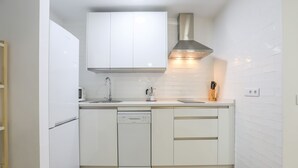 Eine moderne Küche mit weißen Schränken, einem Geschirrspüler, einer Edelstahl-Dunstabzugshaube und einer gefliesten Rückwand.