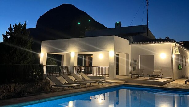 Ein moderner Poolbereich mit einem klaren, blauen Pool, Liegestühlen und Bergen im Hintergrund.