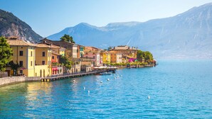 A waterfront town with colorful buildings, a pier, and mountains in the background. - Appartamento Blu Lavanda With Lakeview (Gargnano)