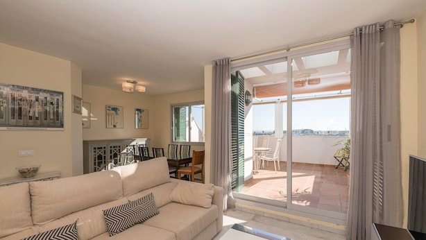 A living room with a beige sofa, a coffee table, and a view of the outdoor patio through a sliding glass door. - Bajamar Deluxe in El Puerto de Santa Maria (El Puerto de Santa Maria)