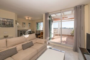 Een woonkamer met een beige bank, een salontafel en uitzicht op het buitenterras door een schuifdeur van glas.