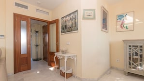 A hallway with a wooden door, a coat rack, a white table with a basket, and a cabinet with glass doors. - Bajamar Deluxe in El Puerto de Santa Maria (El Puerto de Santa Maria)
