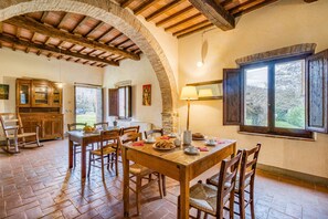 A rustic dining area with a wooden table and chairs, a stone fireplace, and a view of the outdoors through a window. - Molino Felice Among Greenery (Civitella in Val di Chiana)
